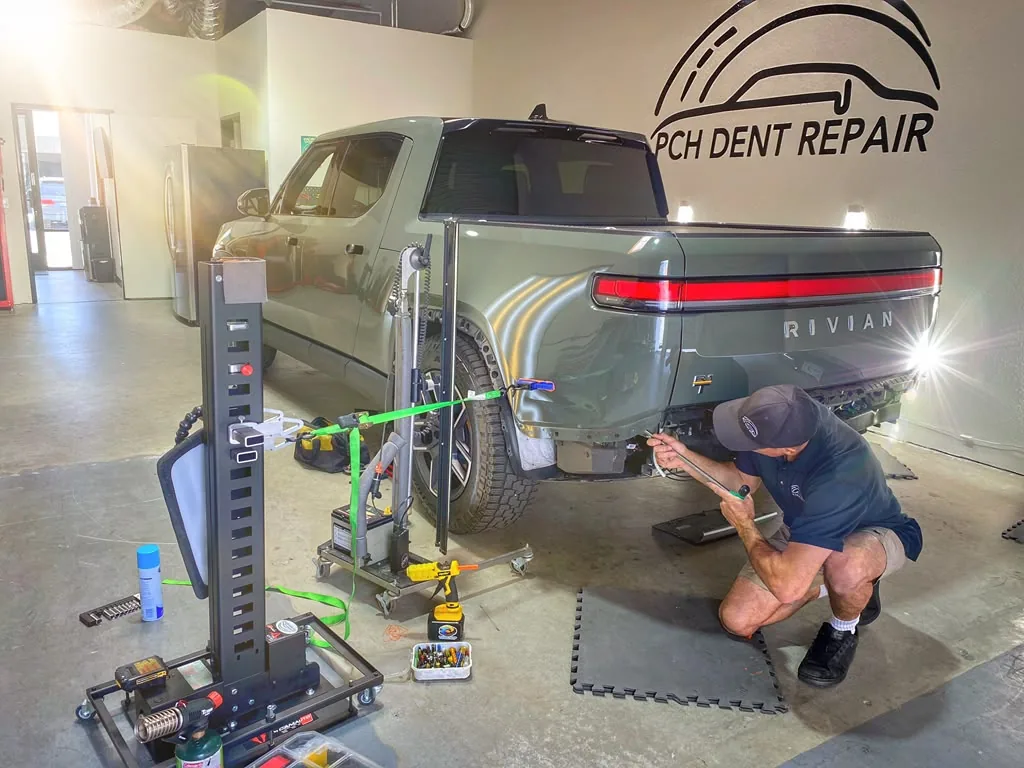 Technician repairing the rear quarter panel of a green Rivian truck with PDR tools