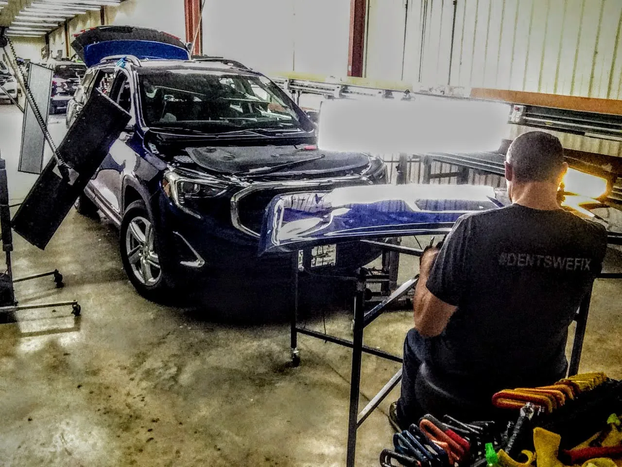 Technician repairing hail dents on a blue GMC hood mounted on a stand