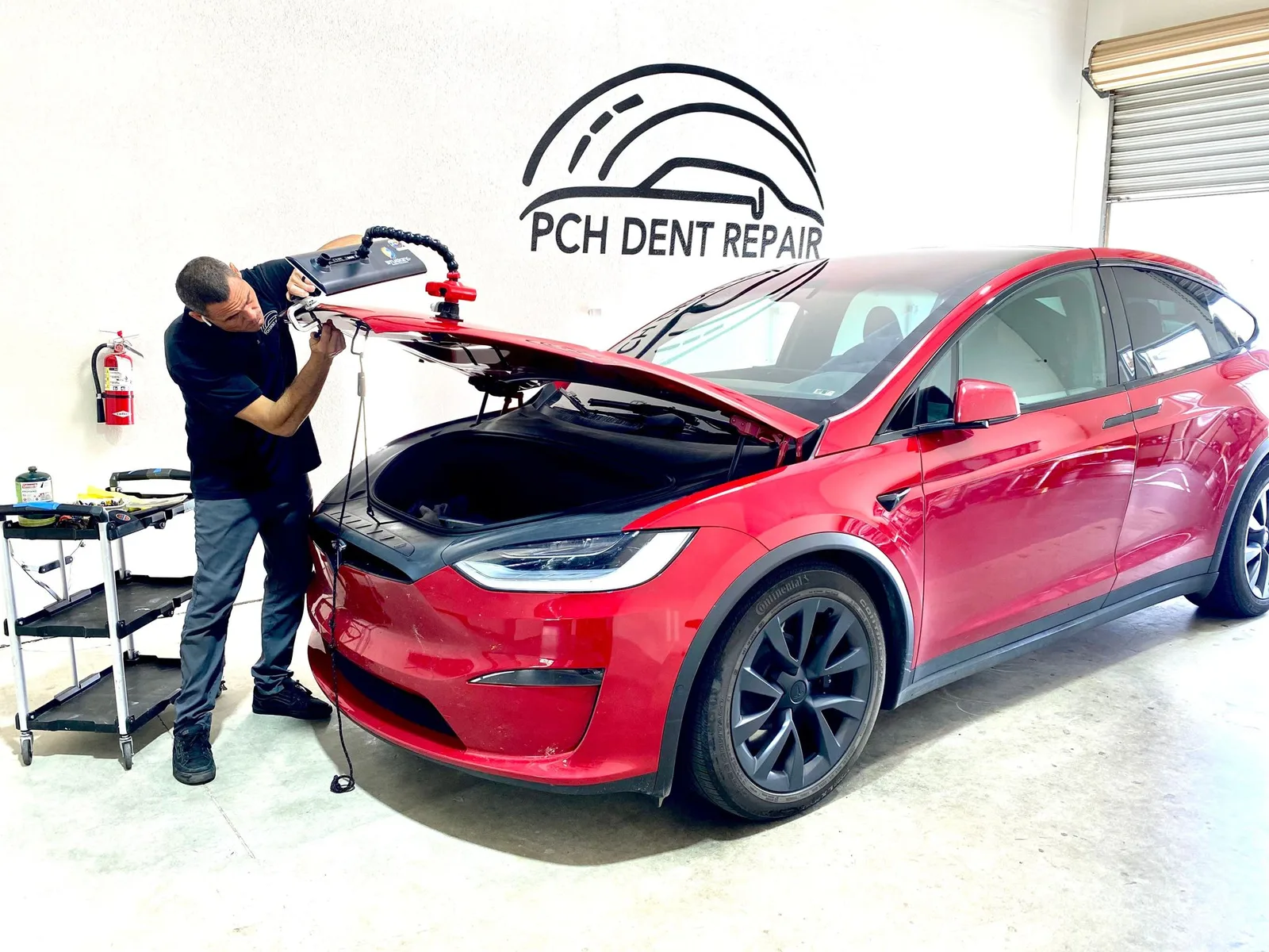 Technician repairing the hood of a red Tesla Model X with a PDR light board